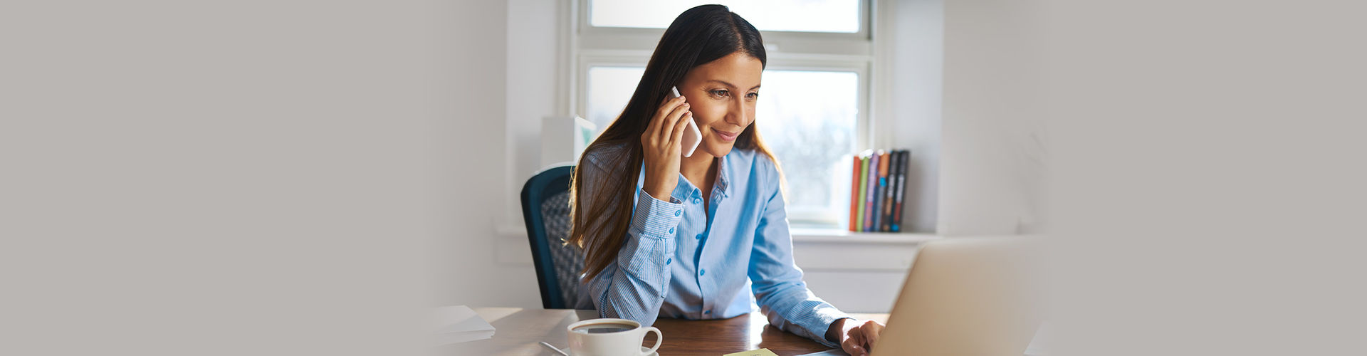 Frau mit Smartphone und Laptop am Schreibtisch