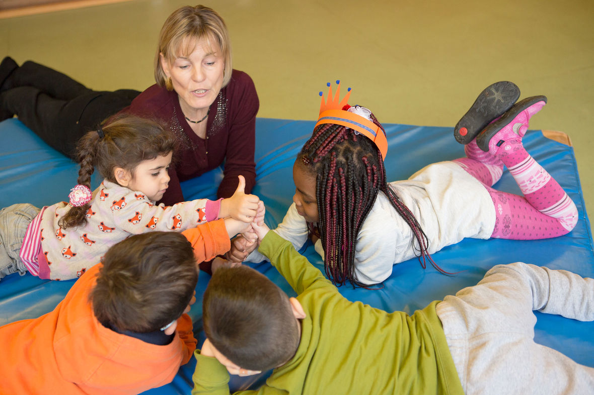 Eine ehrenamtliche Mitarbeiterin beim Sprachlernspiel mit einem Kreis von Kindern